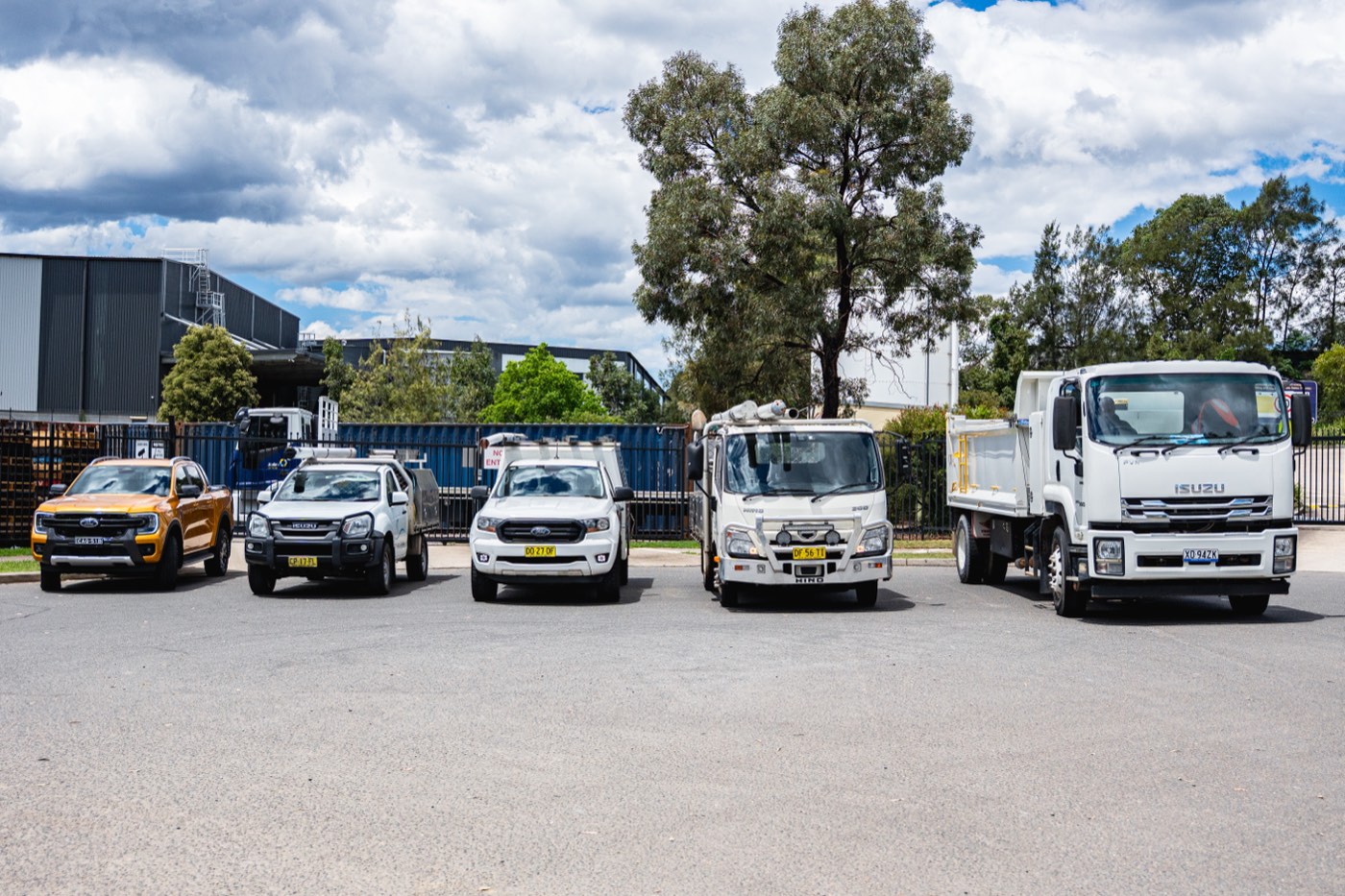 A mixed fleet of trucks and utes parked at a yard under blue sky